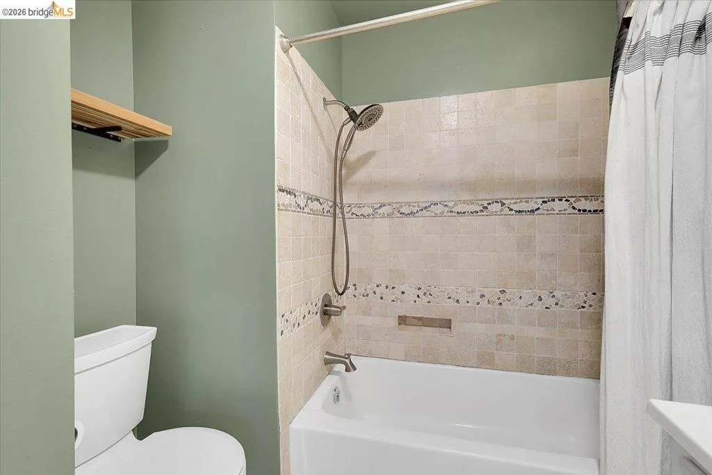 Bathroom featuring a white tub and shower combination with a curved shower curtain rod, a tile surround with decorative accent bands, and a recessed shower niche