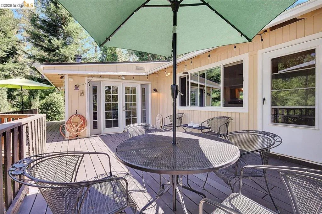 Expansive outdoor deck featuring wood-finish flooring, white-framed French doors, multiple windows, and a railing system
