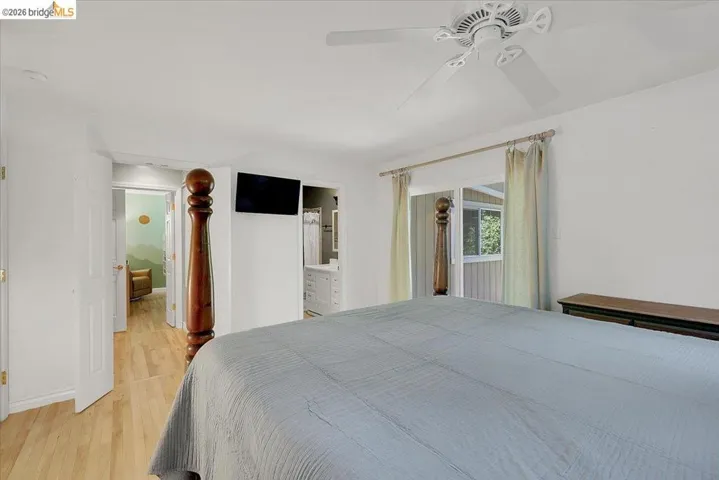 Spacious room featuring wood-finish flooring, a ceiling fan, and white walls