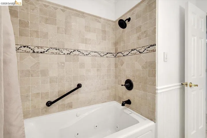 Jetted bathtub with full-height tile surround featuring a decorative mosaic accent band