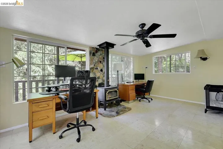 Spacious room featuring multiple windows, a stone-faced fireplace with a wood-burning stove, and tiled flooring