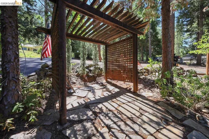 Wood pergola structure with lattice paneling, a flagstone pathway, and mature trees
