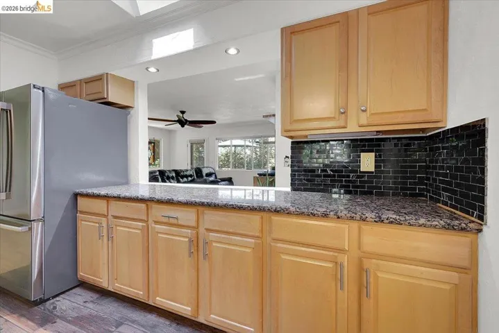 Kitchen featuring wood-finish cabinetry, speckled countertop, and black subway tile backsplash