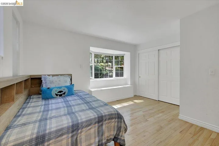 Bright room featuring a bay window with a built-in window seat, light wood-finish flooring, and white sliding closet doors