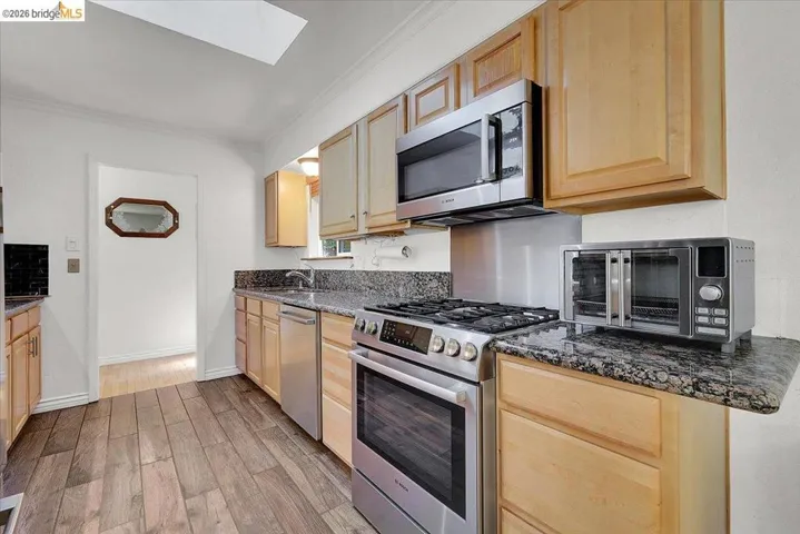 Kitchen featuring wood-finish flooring, light wood cabinetry, granite countertops, and stainless steel appliances including a gas range and microwave