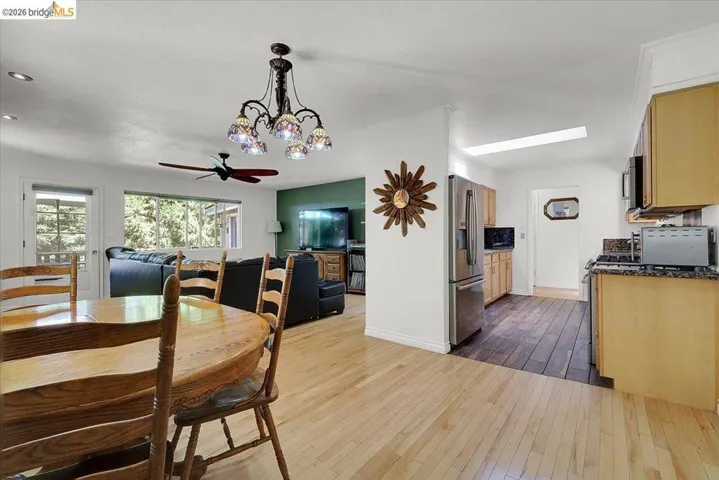 Open concept living and dining area featuring light wood-finish flooring, a decorative ceiling fan, and a multi-shade chandelier