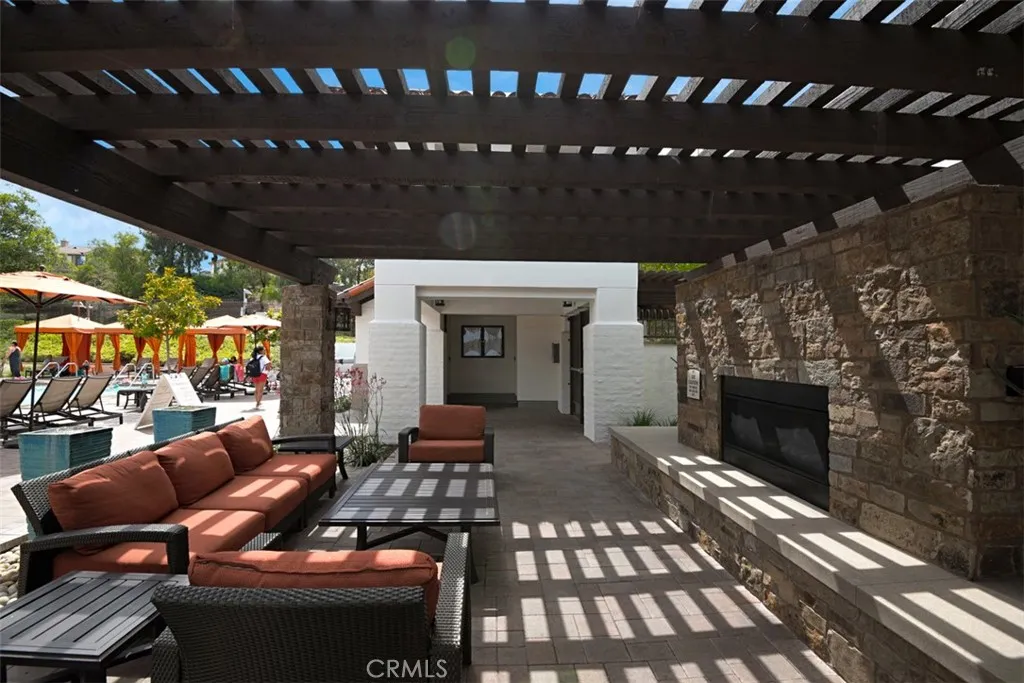 Community Lounge Area: Covered outdoor seating area with a stone fireplace, paver flooring, and pergola-style shade creates a comfortable gathering space near the pool.