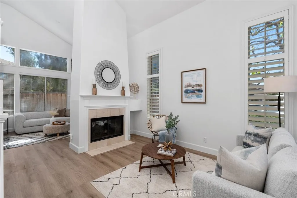 Living Room: Spacious living area with fireplace, tall windows, plantation shutters, and an open connection to an adjacent sitting space.