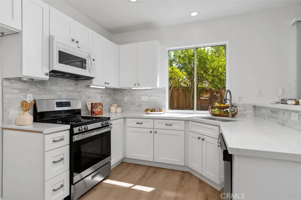 Kitchen: Updated finishes include white cabinetry, light countertops, tile backsplash, stainless-steel range and microwave, and a window above the sink overlooking the backyard.