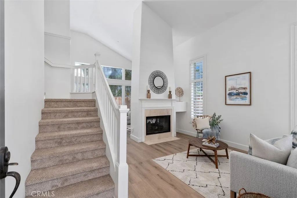 Living Room: Bright living area with vaulted ceilings, wood-look flooring, plantation shutters, and a fireplace with a classic mantel.