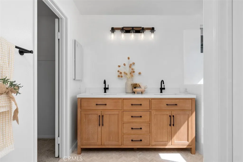 Primary Bathroom: Double-sink vanity with warm wood cabinetry, black fixtures and hardware, and a modern multi-light fixture creates a clean, updated look.
