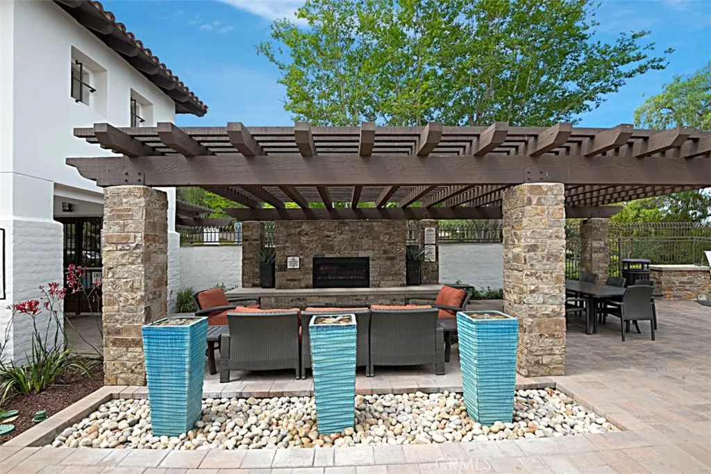 Community Lounge: Pergola-covered lounge with cushioned seating, stone accents, and a fireplace offers a relaxed setting within the community amenities.