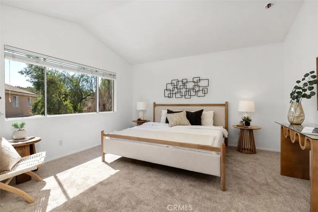 Primary Bedroom: Spacious bedroom with vaulted ceilings, soft carpeting, and a wide window that brings in abundant natural light.