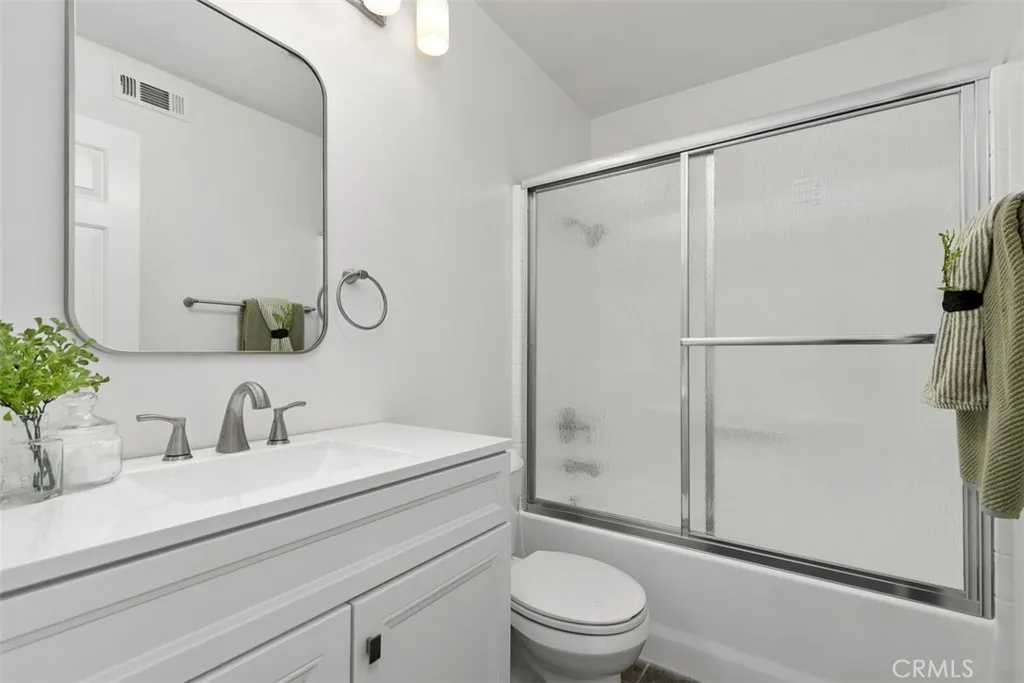 Secondary Bathroom: Full bath with a white vanity, broad mirror, brushed-nickel fixtures, and a tub/shower combination with textured glass doors.