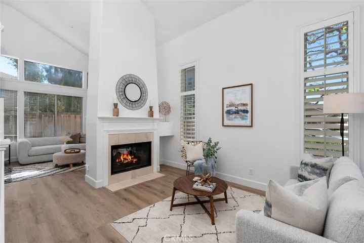 Living Room: Vaulted ceilings, wood-look flooring, plantation shutters, and a fireplace create a bright, polished main living space with an adjoining sitting area.