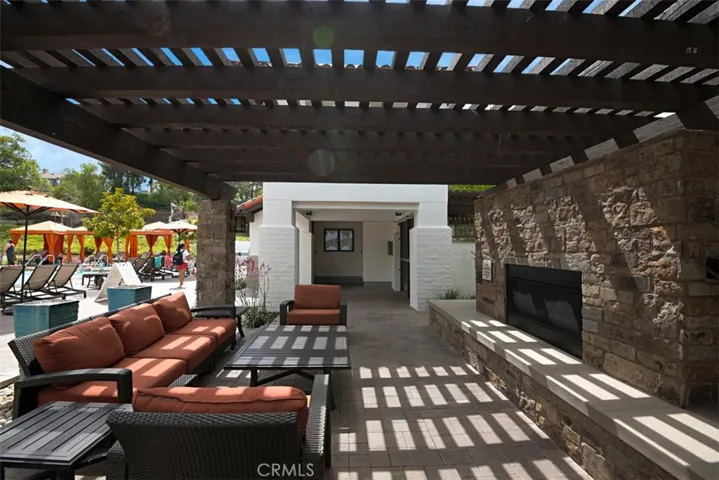 Community Lounge Area: Covered outdoor seating area with a stone fireplace, paver flooring, and pergola-style shade creates a comfortable gathering space near the pool.