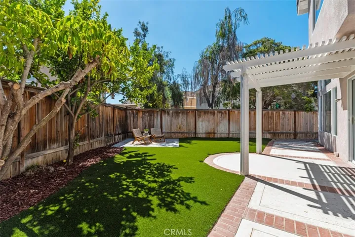 Backyard / Patio: Wide backyard view highlights the shaded patio, brick-accented hardscape, mature trees, and open turf area for flexible outdoor use.