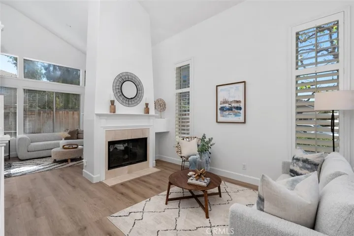 Living Room: Spacious living area with fireplace, tall windows, plantation shutters, and an open connection to an adjacent sitting space.