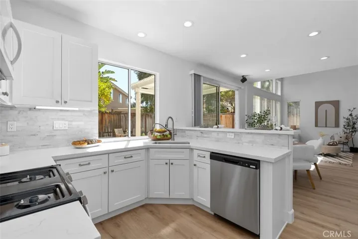 Kitchen: Bright kitchen with white shaker-style cabinetry, solid-surface countertops, tile backsplash, stainless-steel dishwasher, recessed lighting, and a pass-through view toward the adjoining living space.