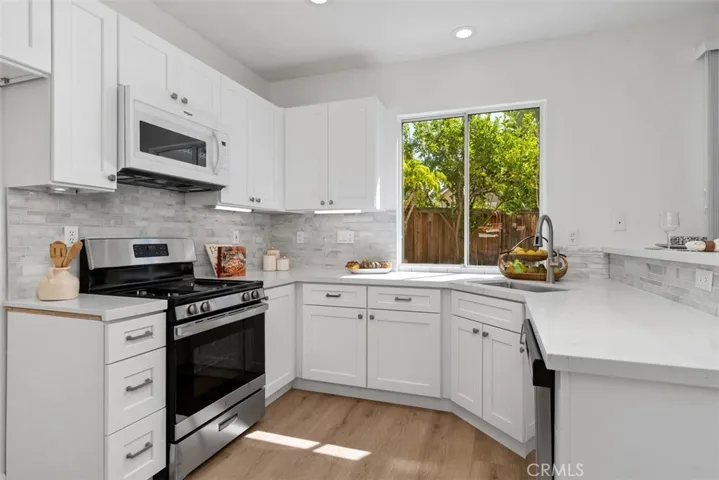 Kitchen: Updated finishes include white cabinetry, light countertops, tile backsplash, stainless-steel range and microwave, and a window above the sink overlooking the backyard.