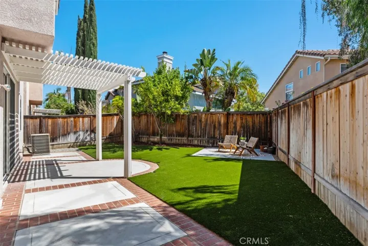 Backyard / Patio: Covered patio with pergola-style shade, brick-accented hardscape, and a turf lawn creates a versatile outdoor entertaining space.