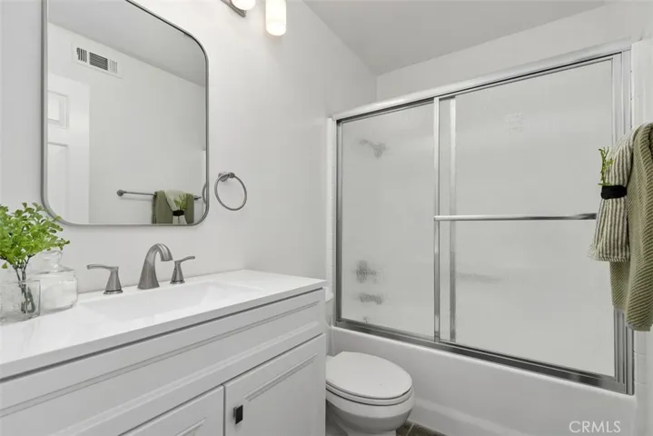 Secondary Bathroom: Full bath with a white vanity, broad mirror, brushed-nickel fixtures, and a tub/shower combination with textured glass doors.
