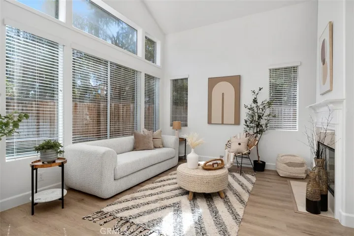 Living Room: Soaring ceilings and a wall of windows fill the room with natural light, while the fireplace and wood-look flooring add warmth and visual interest.