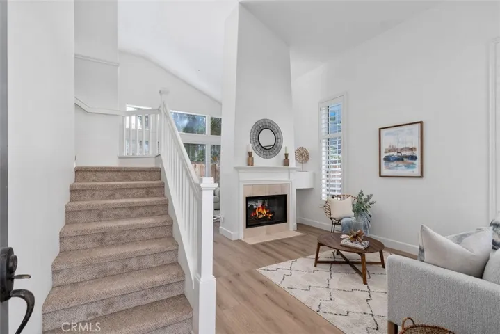 Living Room: Alternate view of the living room showcasing the vaulted ceiling, fireplace focal point, staircase, and abundant natural light.