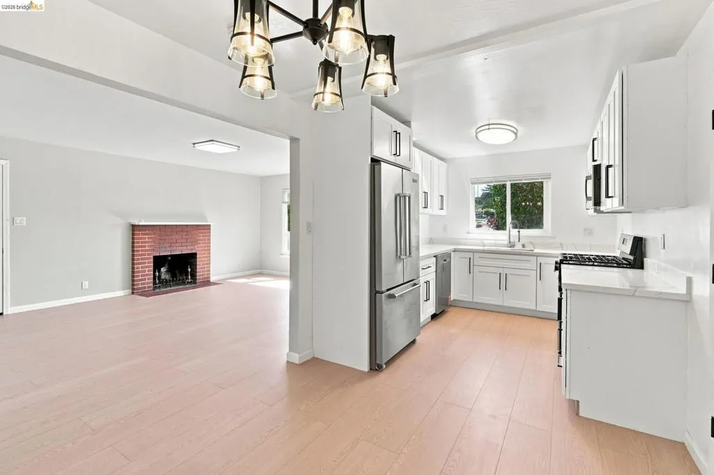 White cabinetry with black hardware, stainless steel appliances, light-toned flooring, and a brick fireplace. White cabinetry with black hardware, stainless steel appliances, light-toned flooring, and a brick fireplace.