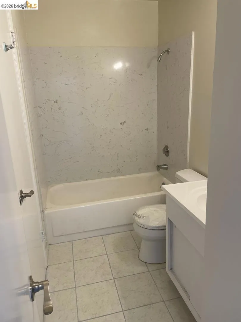 Bathroom featuring a white bathtub with a faux-stone surround, square floor tiles, and a white vanity with an integrated sink