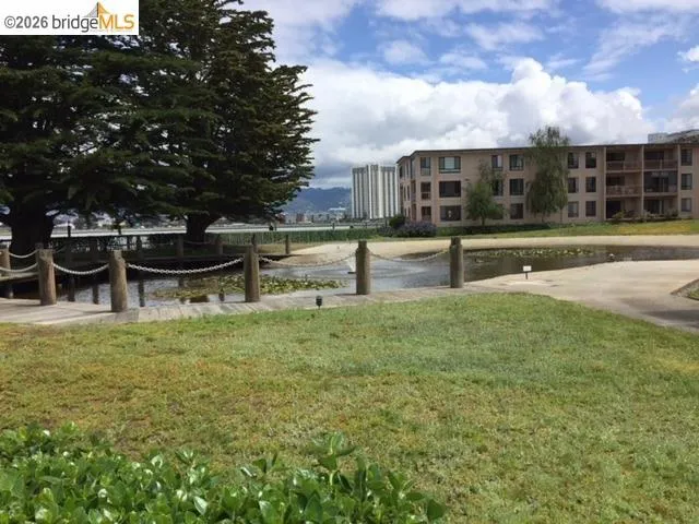 Waterfront setting featuring mature trees, a wooden boardwalk, tranquil water with lily pads, and a manicured lawn area