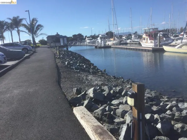 Waterfront setting featuring a paved pathway, rock-lined shore, and boat docks with various vessels
