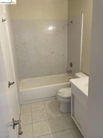 Bathroom featuring a white bathtub with a faux-stone surround, square floor tiles, and a white vanity with an integrated sink