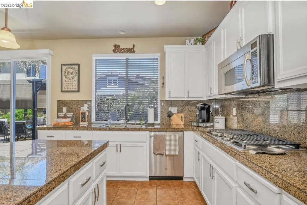Kitchen featuring white cabinetry, granite countertops, stainless steel appliances, a gas range, and a glass sliding door to the exterior