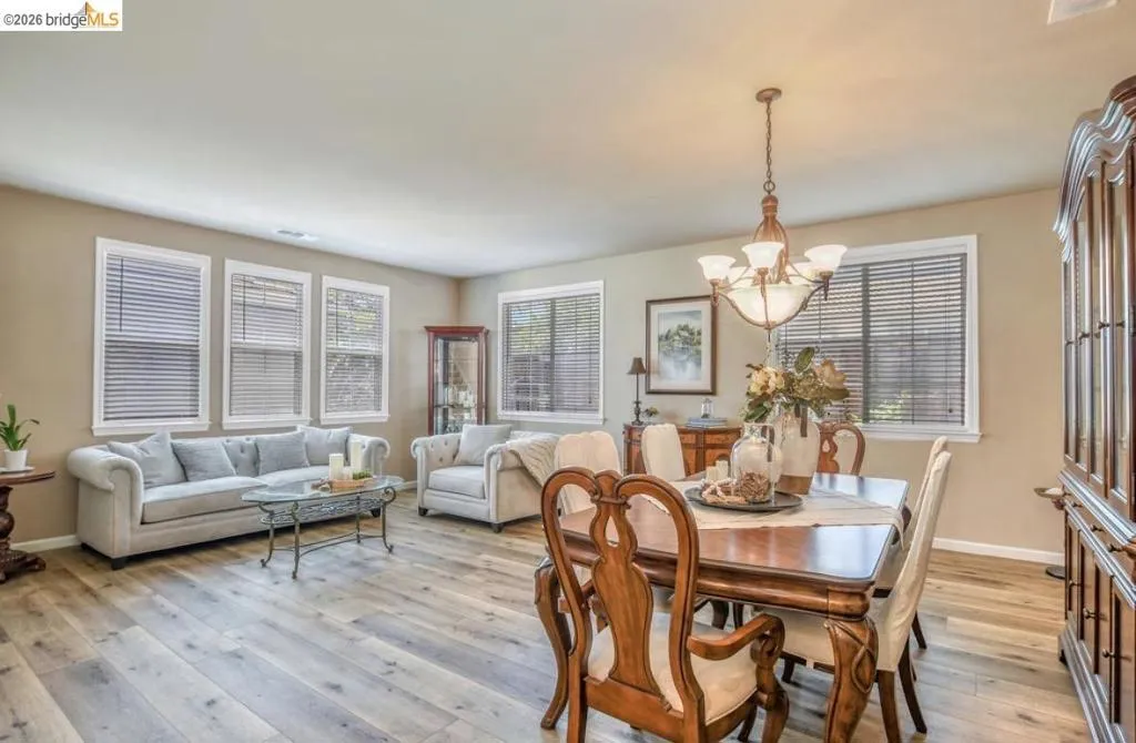Combined living and dining area featuring wood-finish flooring, neutral wall tones, and multiple windows with blinds