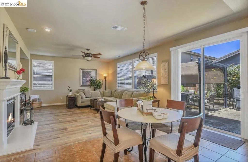 Open-concept living area with wood-finish flooring, a built-in fireplace featuring a white mantle, a ceiling fan, and sliding glass doors leading to an exterior patio