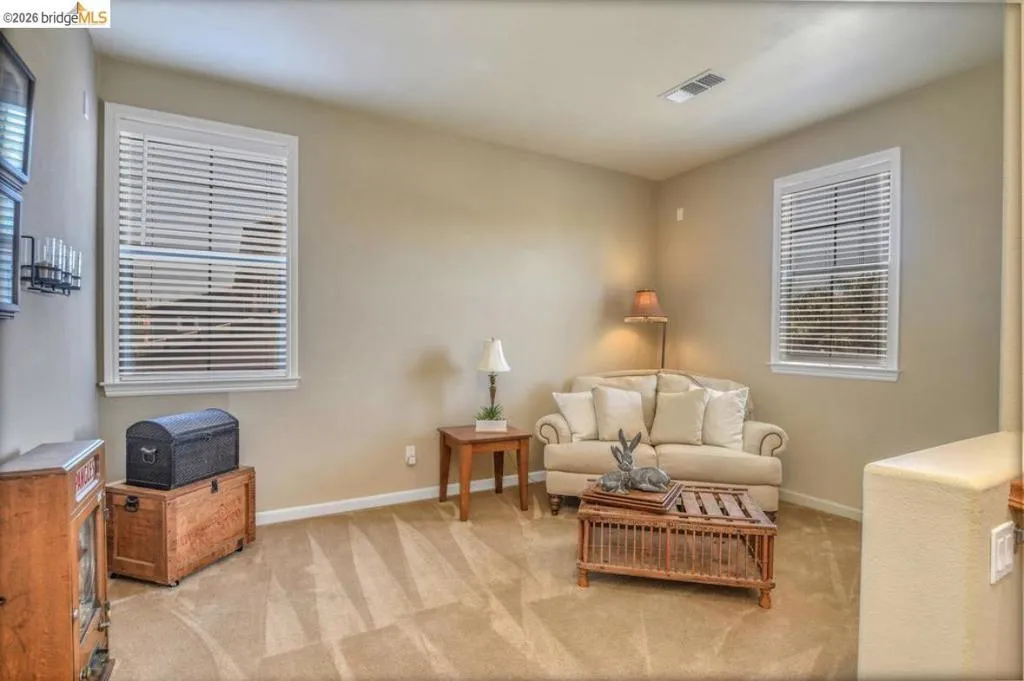 Carpeted room featuring two windows with white blinds, neutral wall paint, and a built-in shelf on the left wall