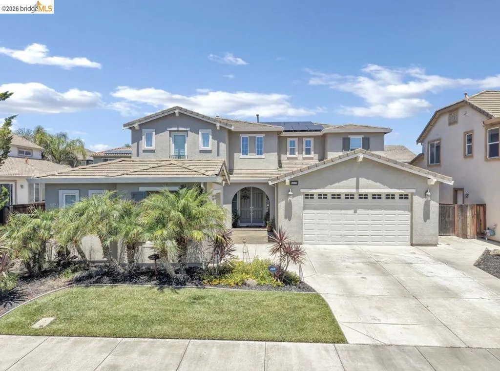 Contemporary stucco exterior featuring a two-car garage, concrete driveway, and mature landscaping