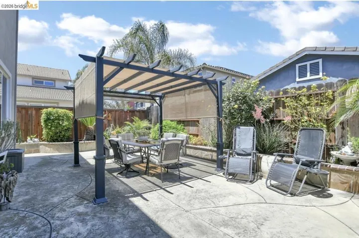 Hardscaped patio featuring a black pergola with a retractable fabric canopy, a raised planter bed with mature landscaping, and privacy fencing