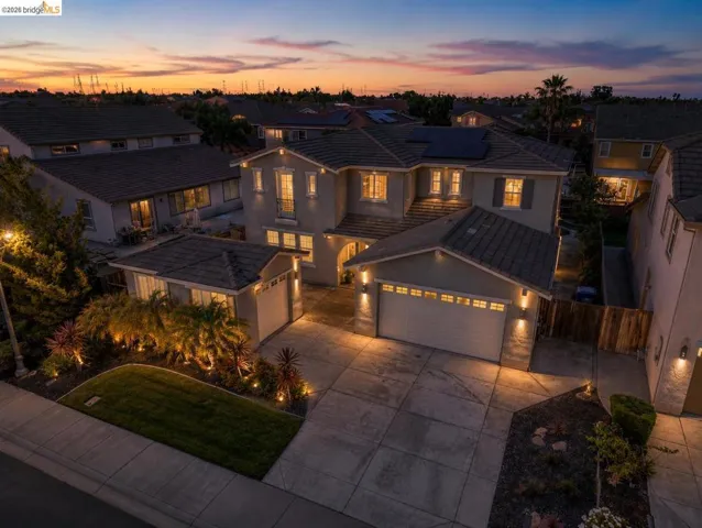 Contemporary two-story stucco residence featuring a tile roof, solar panels, a three-car garage, and extensive exterior accent lighting highlighting mature landscaping