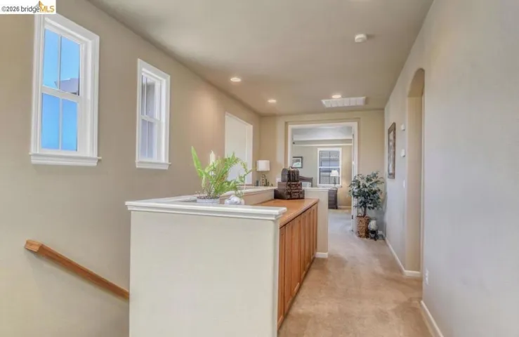 Upper-level hallway featuring a half-wall partition with wood-finish cabinetry, recessed lighting, and an arched doorway
