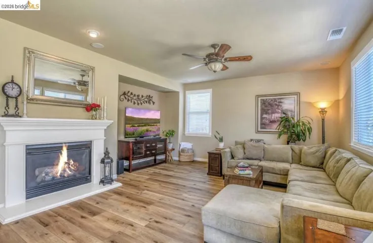 Living area featuring a fireplace with a white mantel, wood-finish flooring, recessed lighting, a ceiling fan, and multiple windows