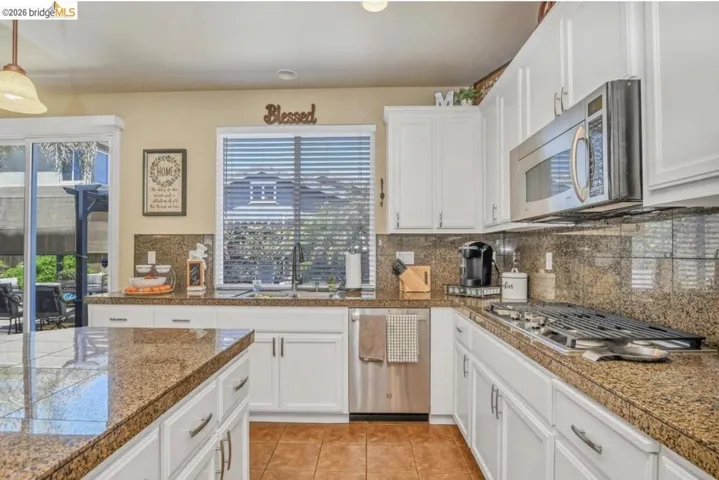 Kitchen featuring white cabinetry, granite countertops, stainless steel appliances, a gas range, and a glass sliding door to the exterior
