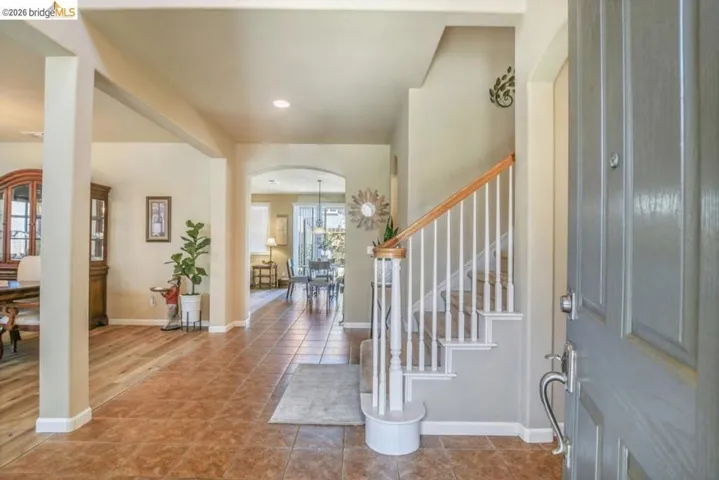 Entryway with a paneled front door, ceramic tile flooring, and a carpeted staircase featuring white balusters and a wood-finish handrail