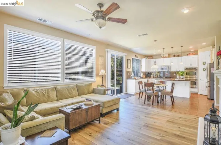 Open-concept living area featuring wood-finish flooring, a ceiling fan, and a kitchen with white cabinetry