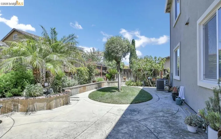 Stamped concrete patio featuring an oval-shaped lawn, surrounded by stone-faced retaining walls and mature landscaping