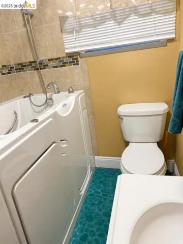 Walk-in tub with chrome fixtures, surrounded by neutral-toned tile with a decorative mosaic accent band