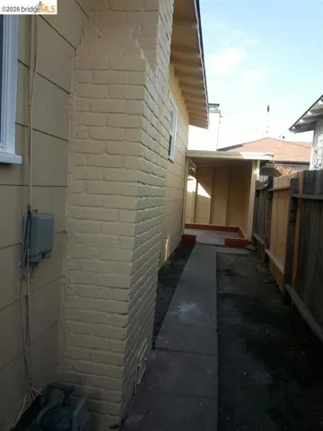 Painted brick chimney and exterior siding with a concrete walkway and wooden fence