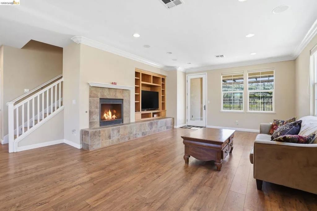 Living area with a tile fireplace, wood-type flooring, ornamental molding, built in features, and recessed lighting