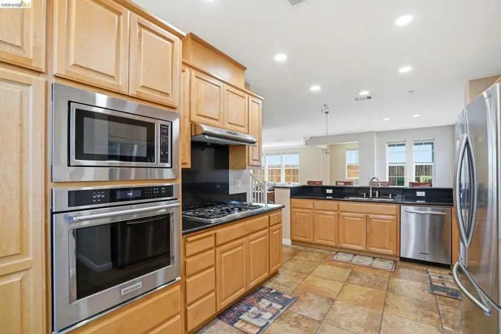Kitchen featuring stainless steel appliances, recessed lighting, light wood finish cabinetry, and dark stone counters